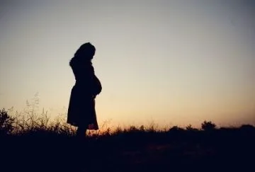 A pregnant woman is silhouetted against the sky.
