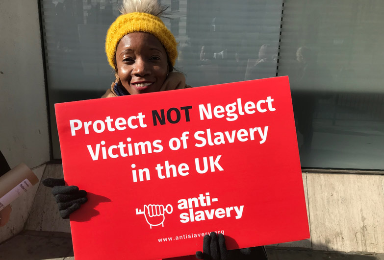 Holding sign that reads protect not neglect victims of slavery in UK