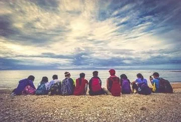 A group of people look out to sea on a stony beach