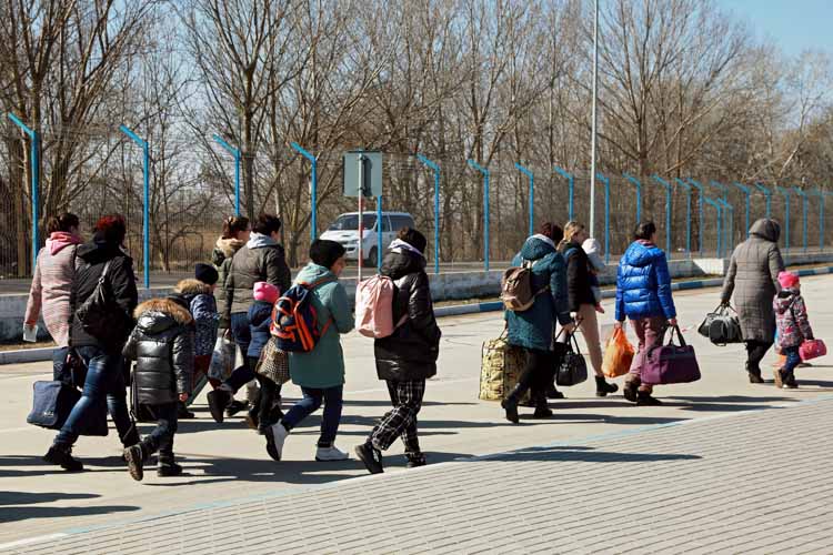 Refugees walking along a road, wrapped up in coats and carrying bags