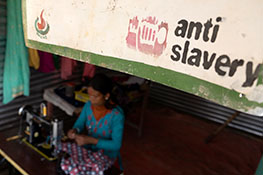 A woman uses a sewing machine below an Anti-Slavery International banner