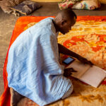 A kneeling man checks a book.