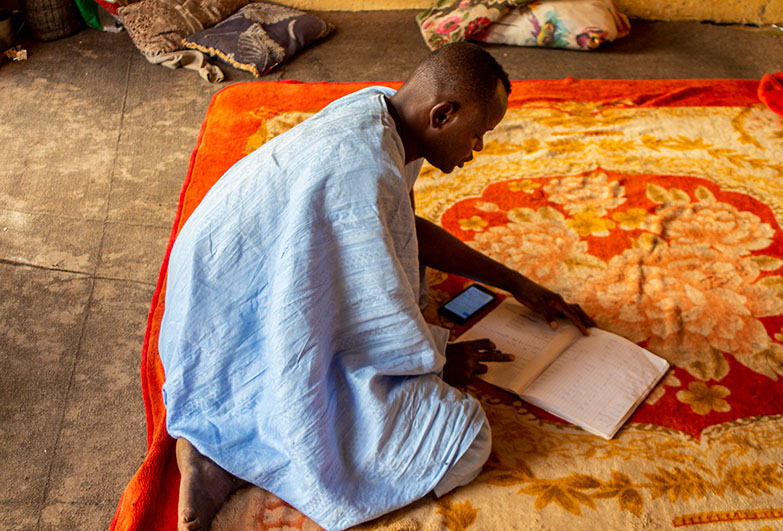 A kneeling man checks a book.