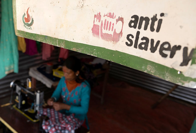 Woman using sewing machine below an Anti-Slavery International banner