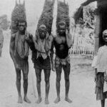 Black and white photo showing three enslaved black men carrying heavy burdens