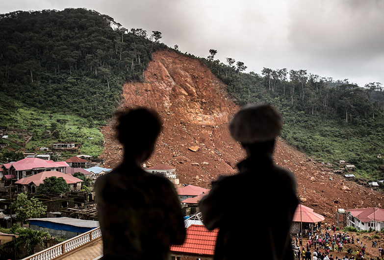 Two women look on to the site where their homes used to be. They are standing on the balcony of a half constructed house where they are now sheltering after a devastating mudslide killed hundreds of people