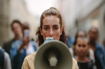 A woman at the front of a crowd speaks into a megaphone