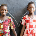 Two girls holding hands in front of a chalkboard