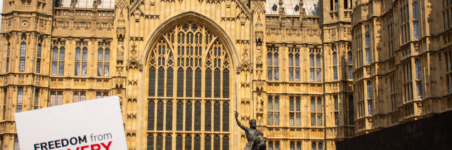 Sign with Anti-Slavery International's logo being held outside the Houses of Parliament, UK