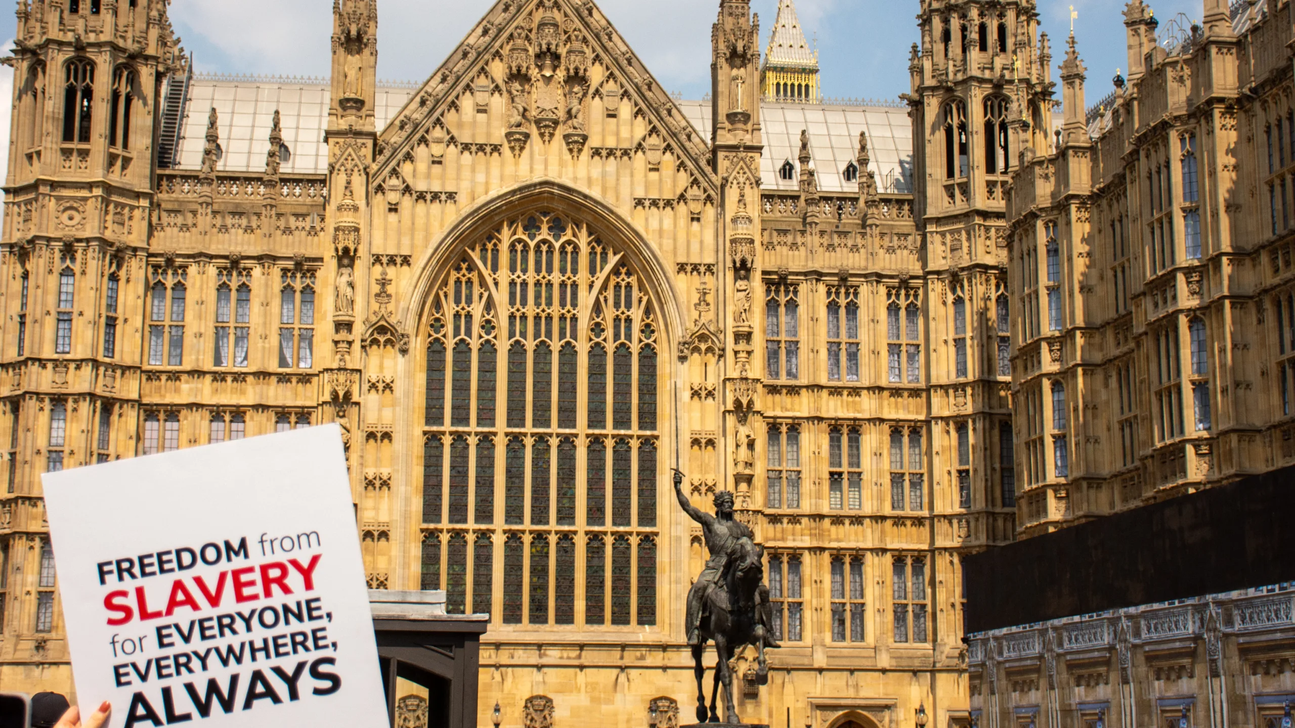 Sign with Anti-Slavery International's logo being held outside the Houses of Parliament, UK