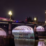 A projection on Westminster Bridge that reads "Slavery Never Ended"
